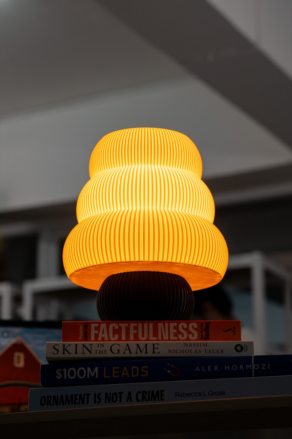 A lit Kumo lamp glowing warm on a stack of books in a dark room